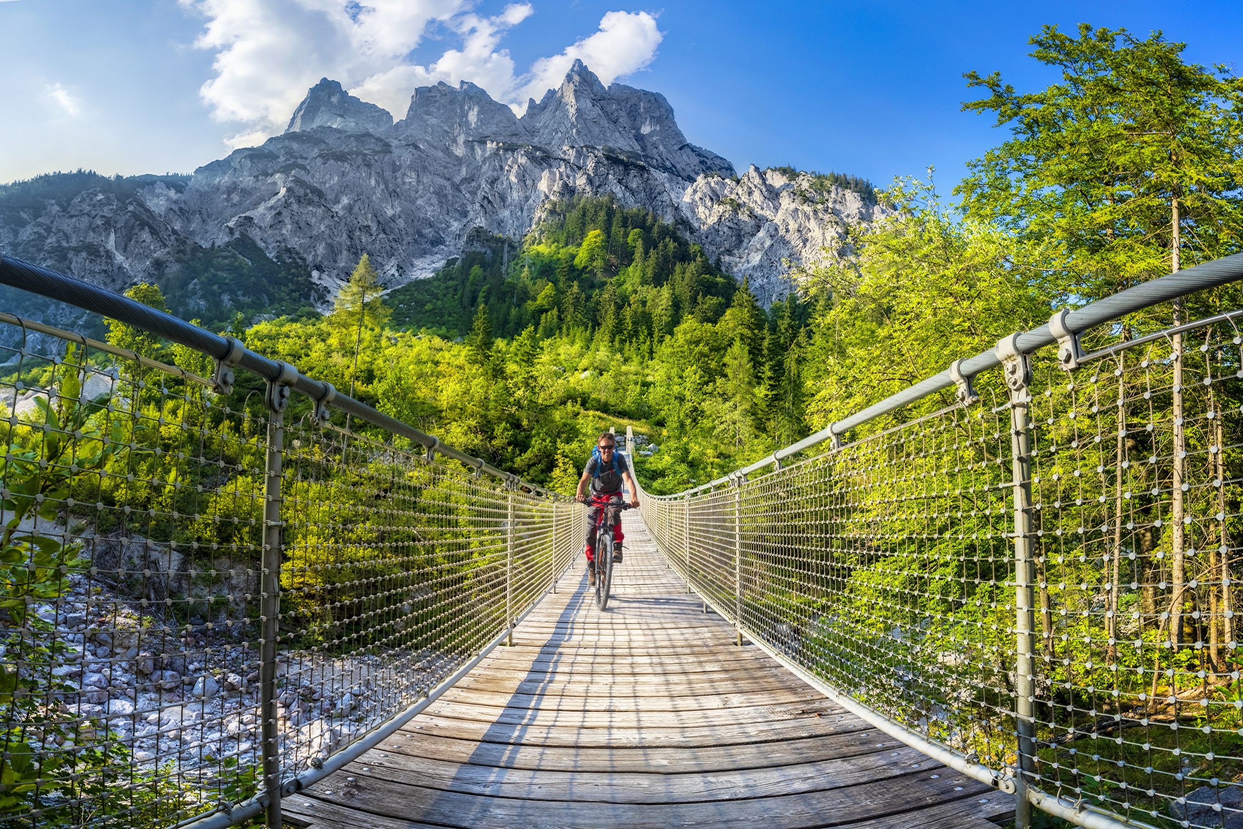 L'été au chalet | GettyImages 1024243592 scaled Mountain biker crossing suspension bridge in the Alps